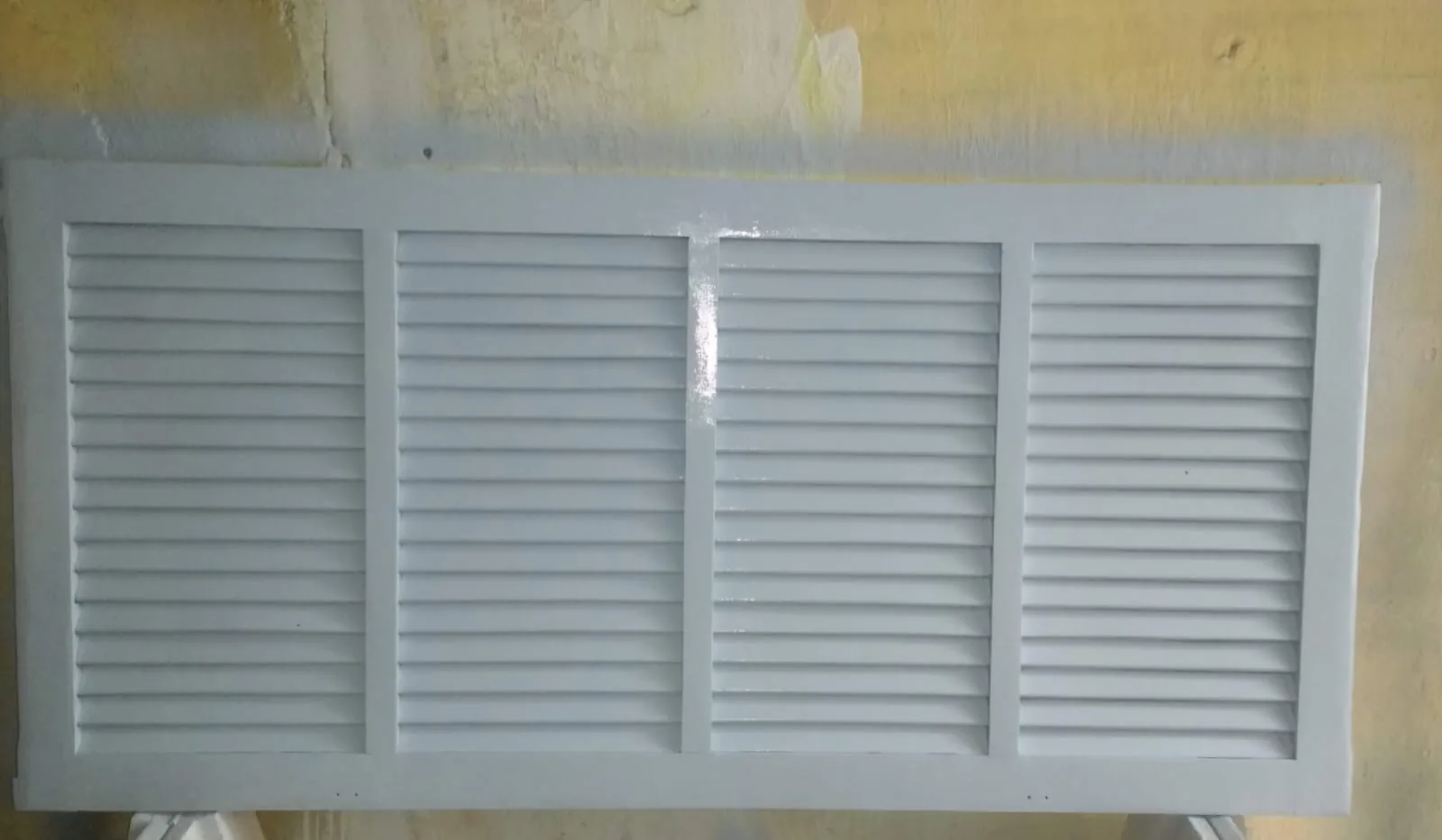 Folha de veneziana de madeira lixada e pintada de branco, apoiada após o acabamento